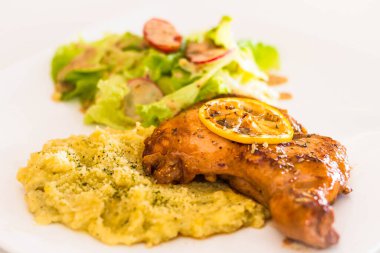 Kızarmış limonlu kırmızı biberli tavuk pirzolası patates püresi ve karışık yeşillikle servis edilir.