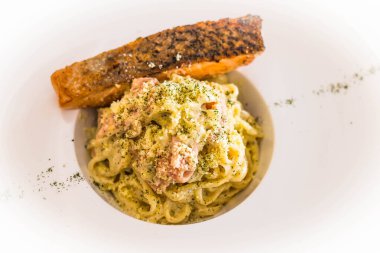 ızgara somon spagetti carbonara ve jambon ve krem sosla servis edilir ve rendelenmiş peynir