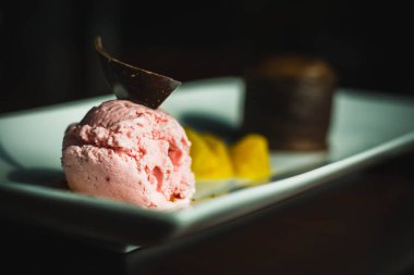 Bir tatlı tabağı çilekli dondurma, üstünde çikolata ve çikolatalı lav keki.