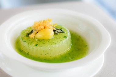 Ispanak soslu haşlanmış karpuzun ana yemeği üzerine beyaz bir kasede servis edilen gingko fındığı.