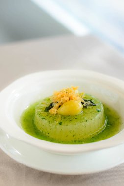 Ispanak soslu haşlanmış karpuzun ana yemeği üzerine beyaz bir kasede servis edilen gingko fındığı.