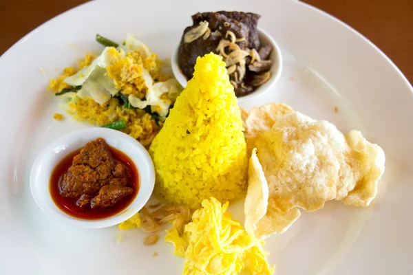 Nasi sárga indonéz sárga rizzsel tálalva párolt marhahús, reszelt tojás, zöldség, kókusz saláta, házi sambal és sós keksz. — Stock Fotó