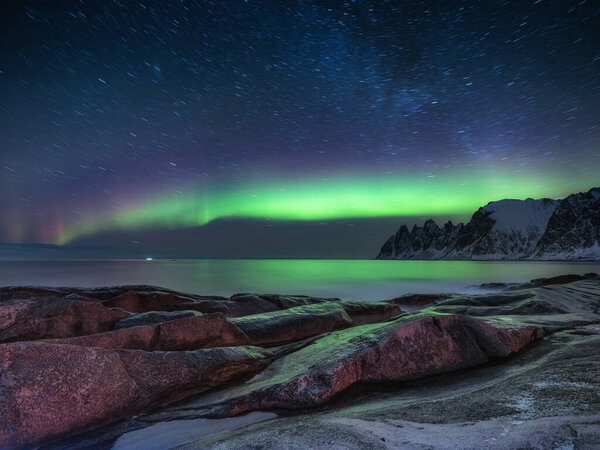 Tungeneset rocks and Aurora Borealis light. Stars trails and northern light. Reflections on the water surface. Senja islands, Norway. Travel - image