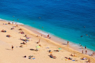Kumsalda ve şemsiyelerde hava manzarası. Tatil ve macera. Kumsal ve mavi su. Kumsaldaki ve gök mavisi denizdeki İHA 'nın üst görüntüsü. Seyahat ve rahatlama videosu