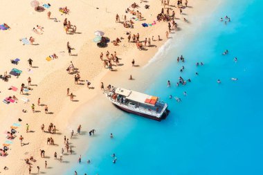 Yunanistan 'ın Zakynthos Adası' ndaki Navagio plajı manzarası. İnsanlar tatilleri sırasında plajda dinleniyorlar. Mavi deniz suyu. Bir tekne insanları deniz kıyısına bırakır. Havadan gelen yaz manzarası.