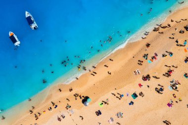 Yunanistan 'ın Zakynthos Adası' ndaki Navagio plajının hava manzarası. İnsanlar tatilleri sırasında plajda dinleniyorlar. Mavi deniz suyu. Bir tekne insanları deniz kıyısına bırakır. İnsansız hava aracından yaz manzarası.