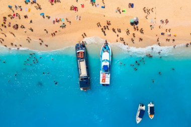 Yunanistan 'ın Zakynthos Adası' ndaki Navagio plajının hava manzarası. İnsanlar tatilleri sırasında plajda dinleniyorlar. Mavi deniz suyu. Bir tekne insanları deniz kıyısına bırakır. İnsansız hava aracından yaz manzarası.