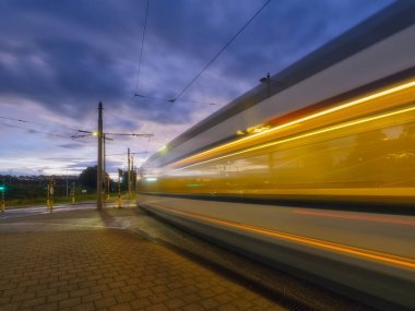 Tramvay durağı. Gün batımında toplu taşıma ve gökyüzü. Tramvay hareket ederken bulanık ışıklar. Ulaşım. Kartpostallar, duvar kağıtları ve arka planlar için fotoğraf.