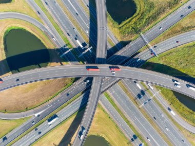 Yoğun araba trafiğiyle çok katlı bir otoyol kavşağının havadan görüntüsü. Modern şehir altyapısı, yol kavşağı ve şehir ulaşım sistemi yukarıdan. Gündüz vakti karmaşık bir köprü ağında hareket eden araçların insansız hava aracı görüntüleri