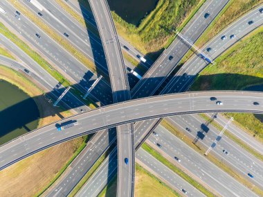 Yoğun araba trafiğiyle çok katlı bir otoyol kavşağının havadan görüntüsü. Modern şehir altyapısı, yol kavşağı ve şehir ulaşım sistemi yukarıdan. Gündüz vakti karmaşık bir köprü ağında hareket eden araçların insansız hava aracı görüntüleri