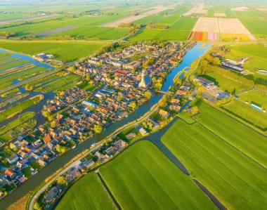 Hollanda 'nın kırsal bir köyünün çarpıcı yatay hava görüntüsü. Geleneksel evler, dar kanallar ve parlak güneşli bir gökyüzünün altında simetrik tarım alanları. Otantik Hollanda manzarası.