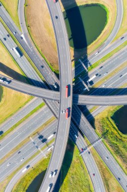 Yoğun araba trafiğiyle çok katlı bir otoyol kavşağının havadan görüntüsü. Dikey fotoğraf. Modern şehir altyapısı, yol kavşağı ve şehir ulaşım sistemi yukarıdan. Yollarda hareket eden arabaların insansız hava aracı görüntüleri.