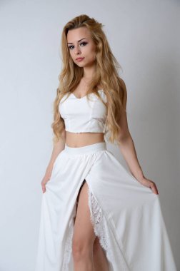 Polonyalı model beyaz bluzlu, uzun beyaz elbiseli, bacaklarını gösteriyor..
