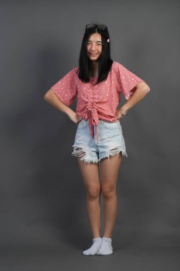 Koyu gri duvarda poz veren genç Asyalı kadın. 