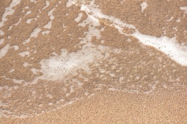 Kumun üzerindeki dalga köpüğü. Dalgaların yakın çekim görüntüsü mükemmel kumlu sahilde yuvarlanıyor..