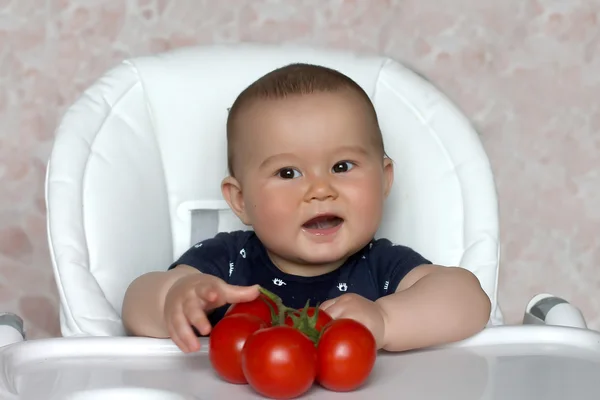 Baby med tomat sitter på stol — Stockfoto