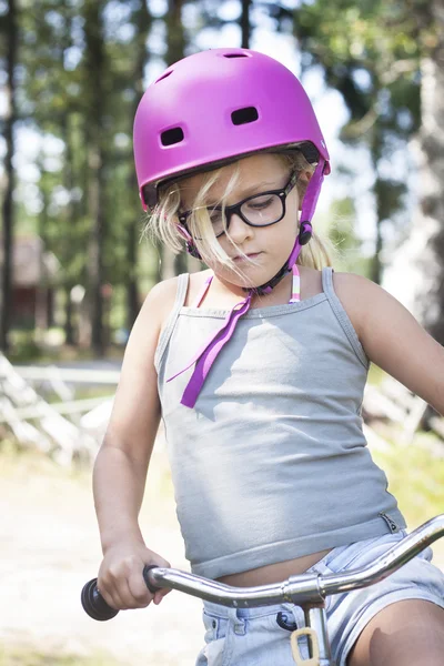 Meisje met roze helm, zwarte glazen en fiets — Stockfoto