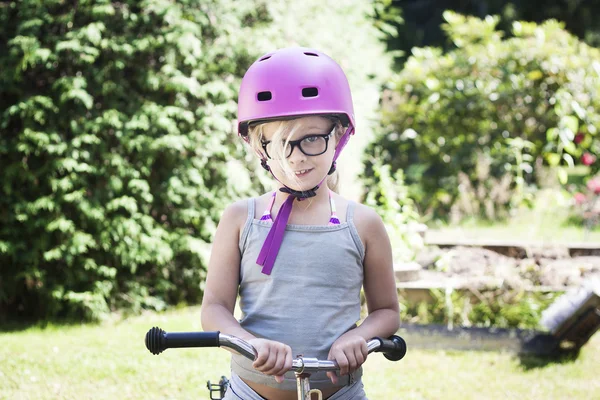 Kind met roze fiets helm en zwarte bril op fiets Rechtenvrije Stockfoto's