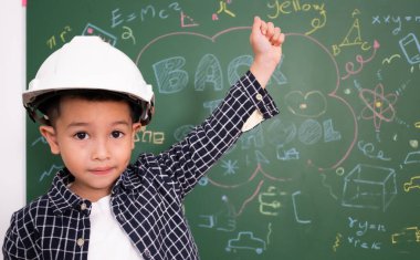 Asyalı küçük çocuk tahtaya beyaz mühendis şapkası takıyor..