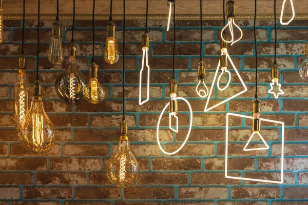 Decorative LED bulbs of various modifications hang from the ceiling against the background of the wall. Vintage and modern style of room lighting.