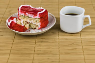 Bir fincan tabakta kırmızı kesim kek ve bambu peçetede bir fincan kahve..