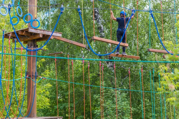A teenager walks along a rope park at a height in safety equipment.