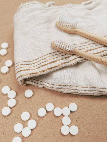 Bamboo toothbrush and dental tabs on a wooden background as a plastic free swap. Zero waste personal care products.