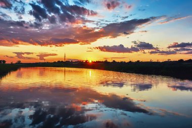 Gölün üzerinde gün batımı karşı kıyının siluetleri. Bulutları suya yansıtan gökyüzü.