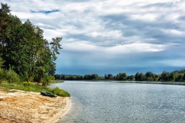 Nehirdeki kumlu sahil ve üzerlerinde bulutlar..