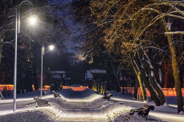 Kış gecesi sokağı karla kaplı. Parkta fener ışıkları yanıyor..