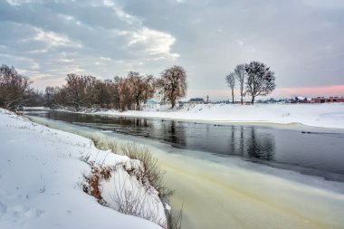 Kış manzarası. Gün batımında ağaçlar ve çalılarla kaplı nehir kıyısı..