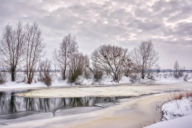 Kış manzarası. Gün batımında ağaçlar ve çalılarla kaplı nehir kıyısı..
