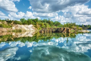 Orman gölünün kıyısı suya yansıyor, gökyüzü bulutlarla kaplı..