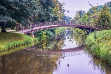 Parkta ağaçların arasında, kanalın karşısındaki yaya köprüsü..