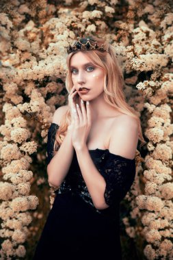 Yeşil arka planda çiçekler olan siyah elbiseli güzel sarışın bayan. Güzelliğin ve sağlıklı yaşam tarzının portresi