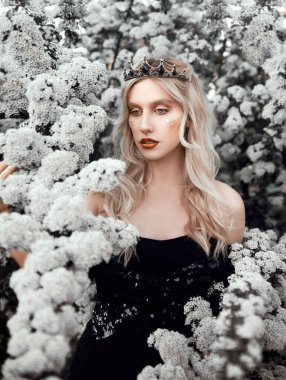 Yeşil arka planda çiçekler olan siyah elbiseli güzel sarışın bayan. Güzelliğin ve sağlıklı yaşam tarzının portresi