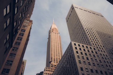 New York, Manhattan 'ın ortasındaki gökdelenler tarafından çevrelenmiş ikonik Chrysler Binası' nın alçak açılı görüntüsü. Dramatik gökyüzüne karşı klasik Art Deco mimarisi.