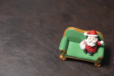 Kahverengi deri arka planda küçük yeşil bir fofanın üzerinde oturan bir Noel Baba mankeni.