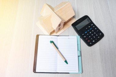 Ahşap ev modeli ve hesap makinesi, defter ve kalemle ahşap zemin üzerinde finans ve iş bankacılığı kavramları.