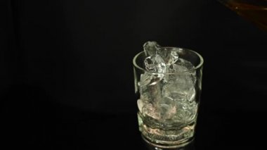 Viskiyi dönen ve hareket eden temiz bir bardağa kopyalama alanı olan siyah bir arkaplan üzerine dökün.