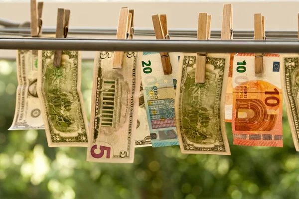 Para aklama kavramı: Dolar ve avro banknotları bulanık yeşil arkaplanda çamaşır iplerinde kurumaya bırakılıyor