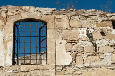 Mavi gökyüzünün önünde metal parmaklıkları olan eski harabe taş duvar.