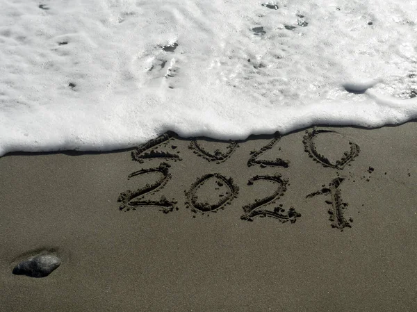 Islak kumsalda 2020 ve 2021 numaralar ve mesajı silmek üzere olan köpüklü bir dalga.