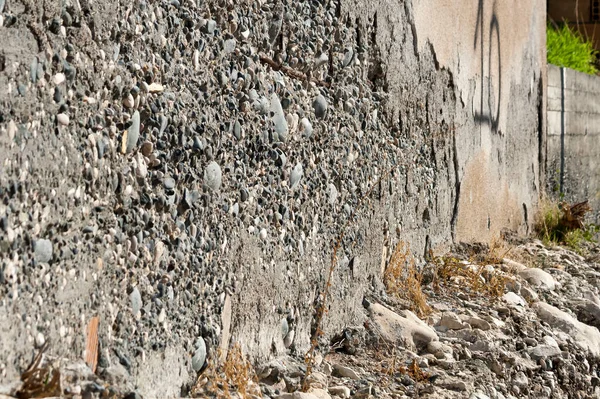 Old rough concrete house wall with peeling plaster in sunlight, angle view