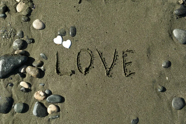 Word Love written on wet sand at the beach among stones in sunlight