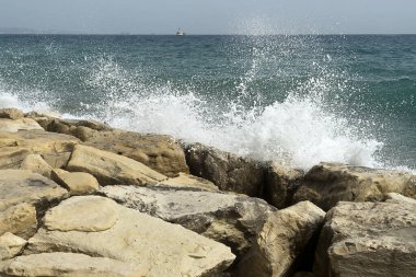 Deniz manzarası ve ufukta görünen gemiler büyük beyaz kayalara çarpıyor.