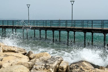 Kıbrıs Rum Kesimi 'nin Limasol kentindeki Molos gezinti güvertesindeki boş yaya köprüsünün önündeki beyaz kayalara su sıçrayan deniz dalgaları 