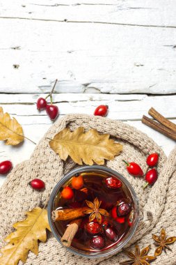Gül kalçalı ve baharatlı bir fincan çayın yakın plan fotoğrafı, sıcak kıyafetler, ahşap arka planda kurumuş yapraklar, üst manzara. Sonbahar konsepti.
