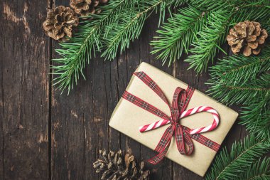 Şeker kamışı, dallar ve koyu kırsal ahşap arka planda çam kozalaklarıyla süslenmiş el işi kağıda sarılı bir hediye kutusu. Metnin için kopyalama alanı olan üst görünüm. Kış tatili kavramı.