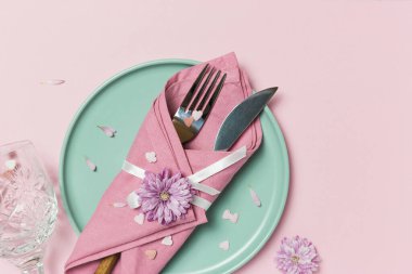 Yeşil tabağı, peçetesi, çiçekleri ve pembe arka planda kalp süslemeleri olan güzel bir sofra. Kopyalama alanı olan üst görünüm.